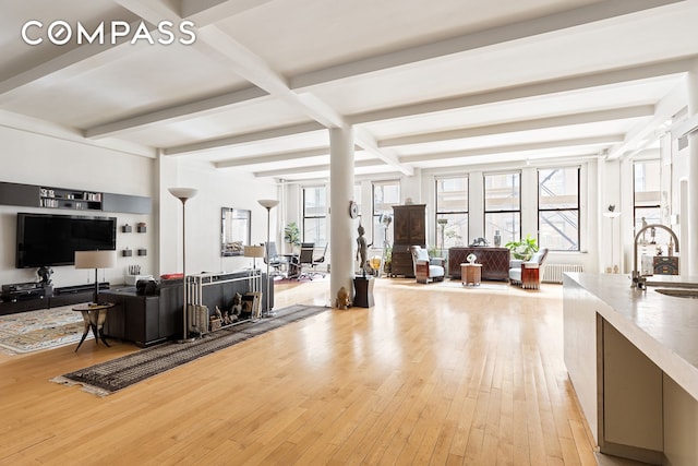 living area featuring light wood finished floors, beam ceiling, radiator heating unit, and a wealth of natural light