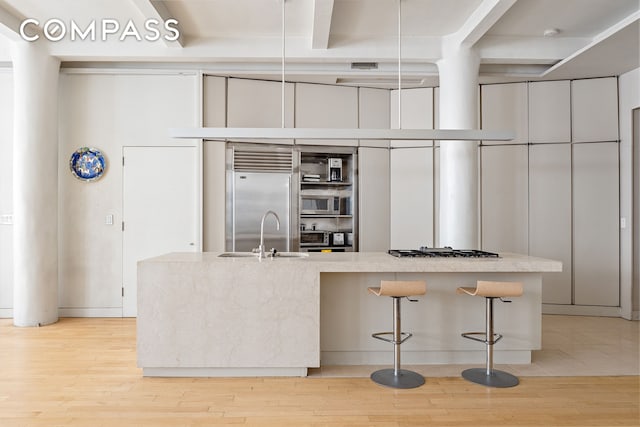 kitchen featuring light wood-type flooring, beamed ceiling, a kitchen bar, a sink, and stainless steel appliances