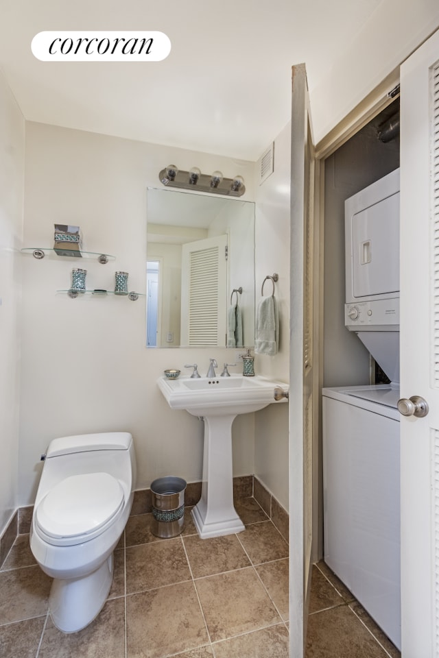 half bath with tile patterned flooring, stacked washer / dryer, toilet, and visible vents