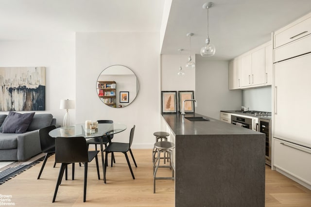 kitchen with dark countertops, beverage cooler, light wood-style floors, white cabinets, and a sink