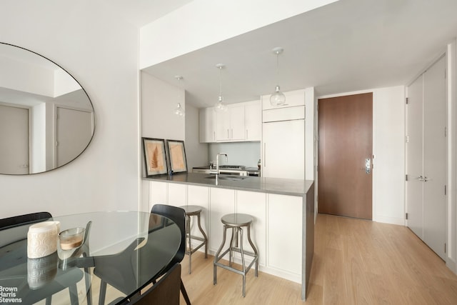 kitchen with light wood-style flooring, a sink, a peninsula, a breakfast bar area, and white cabinets