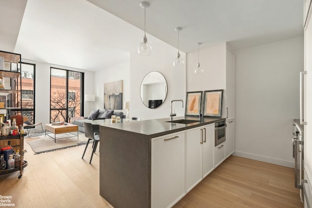 kitchen featuring light wood-style flooring, a sink, dark countertops, a peninsula, and stainless steel oven