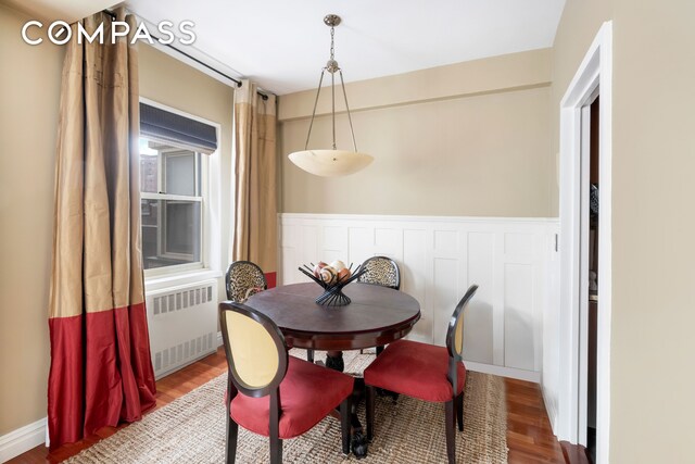 dining space featuring a wainscoted wall, radiator, and wood finished floors