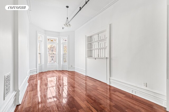 empty room with hardwood / wood-style flooring, a decorative wall, visible vents, and ornamental molding