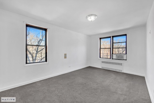 spare room featuring a wealth of natural light, radiator, baseboards, and dark colored carpet