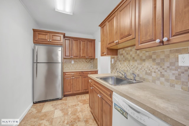 kitchen featuring brown cabinetry, white dishwasher, freestanding refrigerator, and a sink