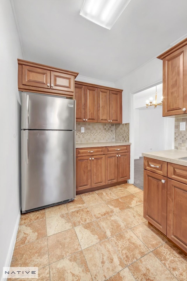 kitchen with brown cabinetry, an inviting chandelier, freestanding refrigerator, light countertops, and tasteful backsplash