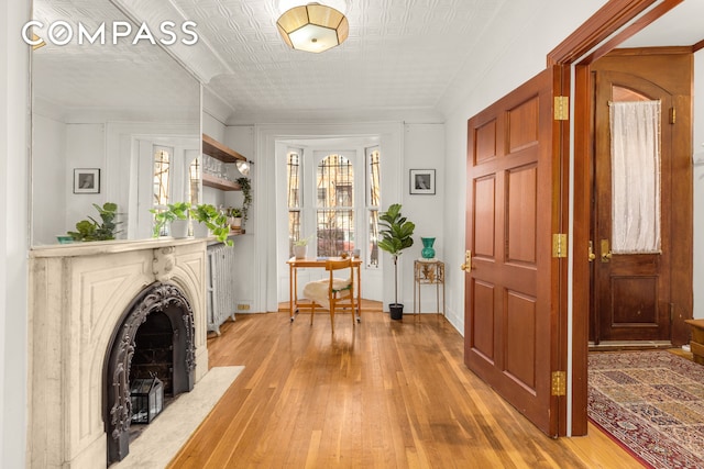 entryway featuring light wood-type flooring, a fireplace with flush hearth, and ornamental molding