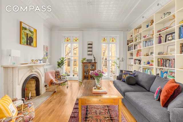 living room with wood finished floors, a fireplace with raised hearth, and an ornate ceiling