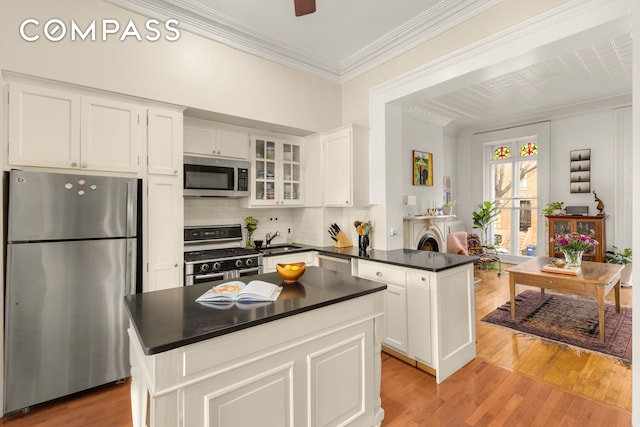 kitchen with dark countertops, ornamental molding, appliances with stainless steel finishes, a peninsula, and a sink