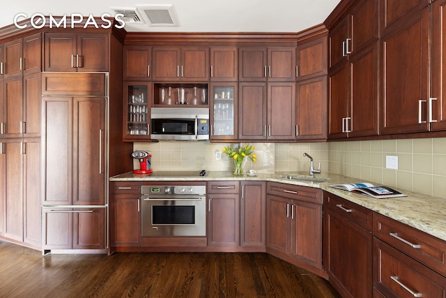 kitchen featuring dark wood finished floors, a sink, stainless steel appliances, glass insert cabinets, and tasteful backsplash