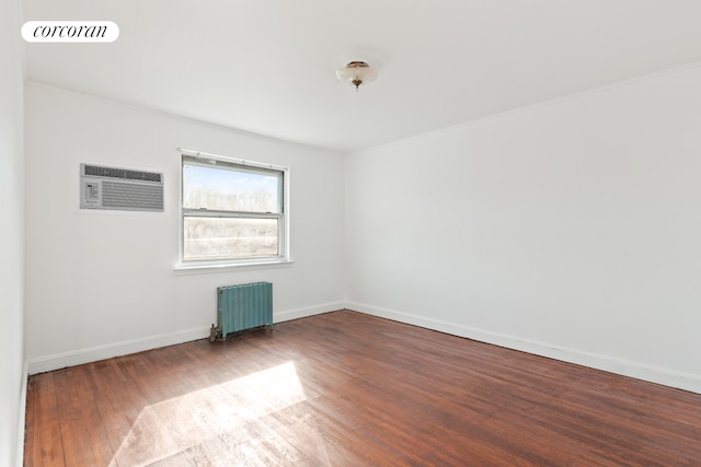 spare room with wood finished floors, visible vents, baseboards, radiator heating unit, and a wall mounted air conditioner