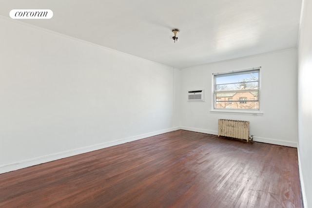 spare room with a wall mounted air conditioner, visible vents, dark wood finished floors, radiator, and baseboards