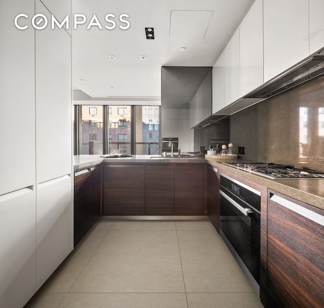 kitchen featuring modern cabinets, a sink, black oven, backsplash, and light tile patterned floors