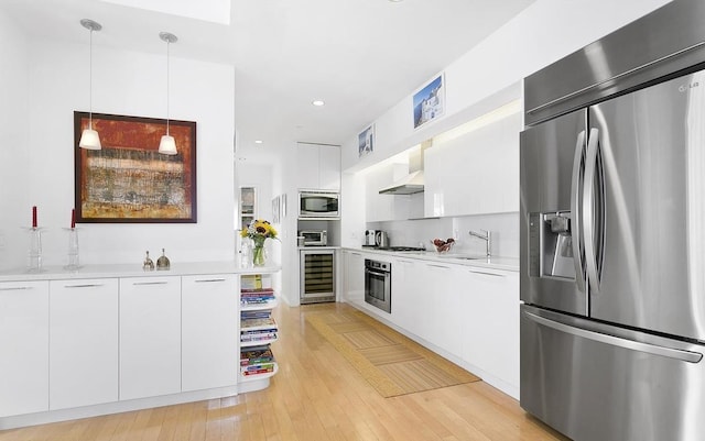kitchen with stainless steel appliances, beverage cooler, light countertops, white cabinetry, and pendant lighting