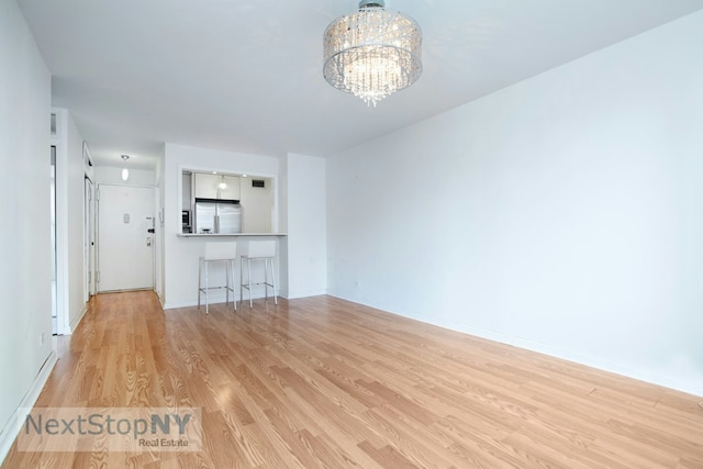 unfurnished living room featuring light wood-type flooring, baseboards, and an inviting chandelier