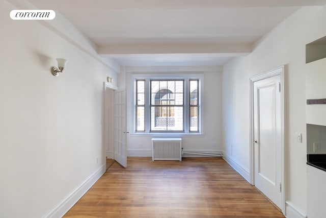 empty room featuring beamed ceiling, radiator heating unit, and wood finished floors