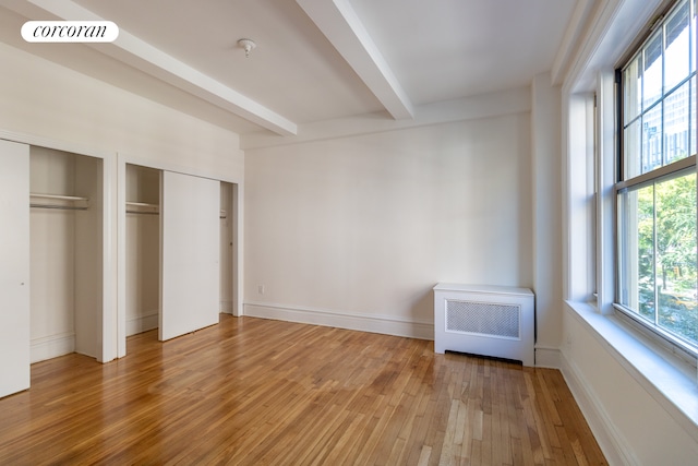 unfurnished bedroom with heating unit, visible vents, beam ceiling, light wood-style floors, and two closets