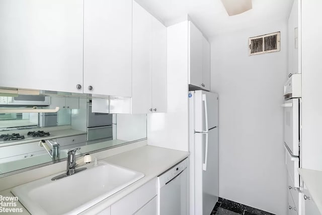 kitchen featuring visible vents, light countertops, white appliances, white cabinetry, and a sink