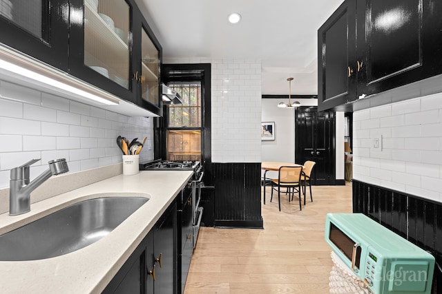 kitchen featuring dark cabinets, light wood-type flooring, light countertops, stainless steel gas range, and a sink