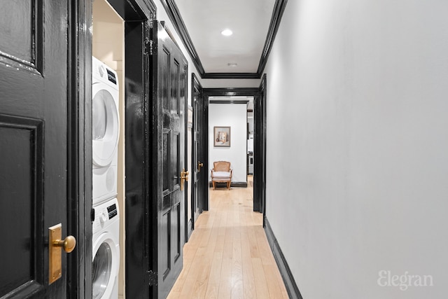 hall with light wood-style flooring, ornamental molding, baseboards, and stacked washing maching and dryer