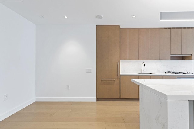 kitchen featuring light wood-type flooring, a sink, backsplash, light countertops, and stainless steel gas cooktop