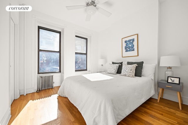 bedroom featuring baseboards, radiator, wood finished floors, and a ceiling fan