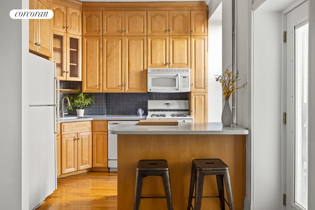 kitchen with a kitchen bar, a sink, backsplash, white appliances, and light wood finished floors