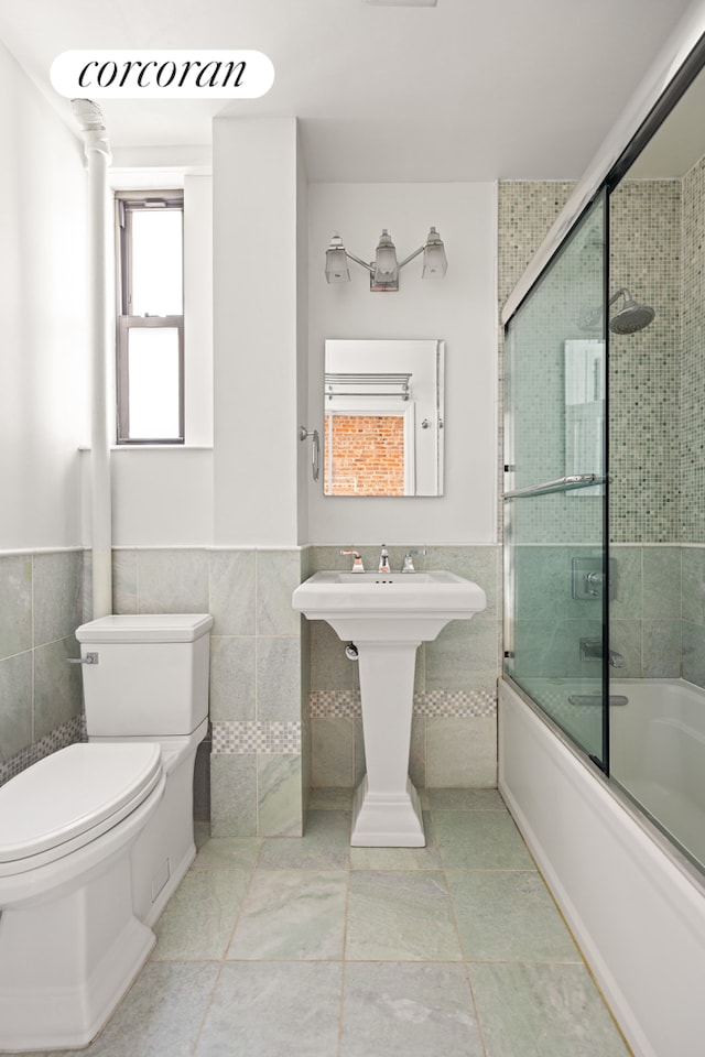 full bathroom featuring a wainscoted wall, enclosed tub / shower combo, a sink, tile walls, and toilet