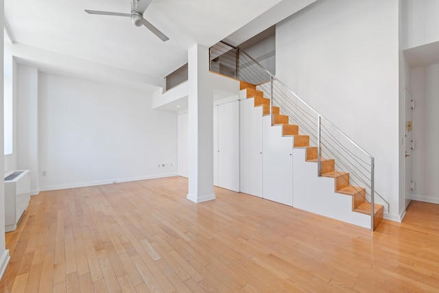 unfurnished living room featuring stairway, baseboards, ceiling fan, and hardwood / wood-style floors