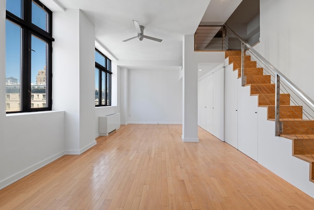 spare room with radiator, light wood-style floors, baseboards, ceiling fan, and stairs