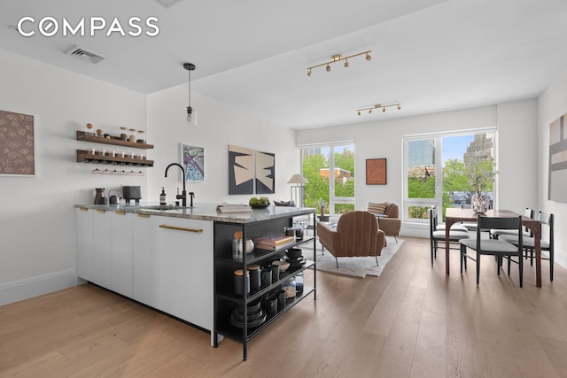 bar featuring baseboards, visible vents, a sink, hanging light fixtures, and light wood-style floors