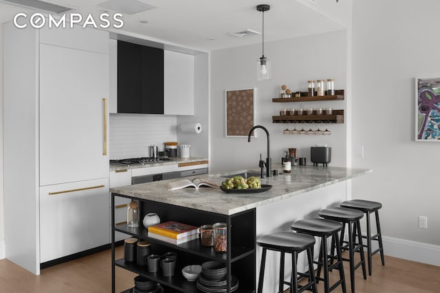 kitchen featuring open shelves, decorative backsplash, a kitchen breakfast bar, gas cooktop, and a sink