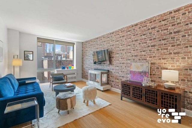 living room with a multi sided fireplace, brick wall, baseboards, and wood finished floors