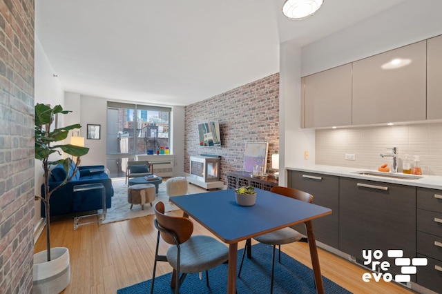 dining area featuring light wood-type flooring, brick wall, and a fireplace