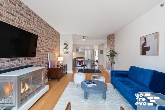 living area with brick wall, baseboards, and light wood finished floors