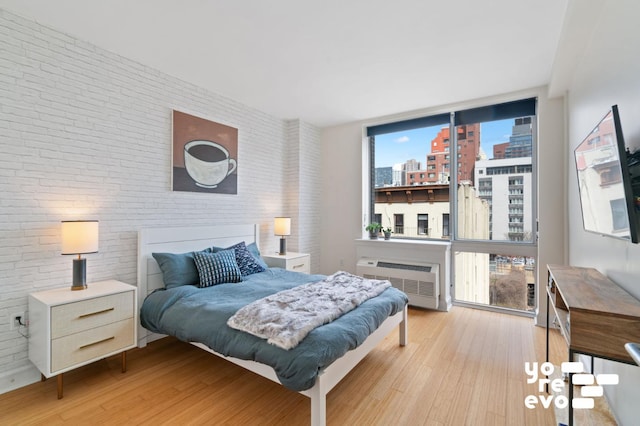 bedroom featuring brick wall, expansive windows, an AC wall unit, and wood finished floors