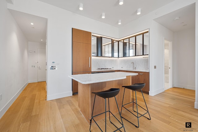 kitchen with brown cabinetry, light wood-style flooring, a kitchen bar, tasteful backsplash, and a center island