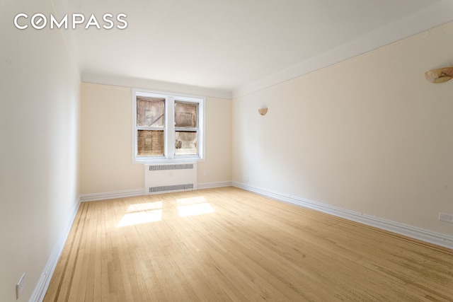 spare room featuring baseboards, radiator, and light wood-style flooring