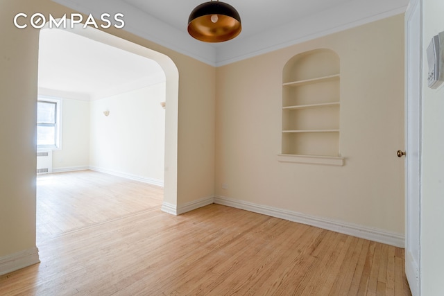 spare room featuring built in features, wood finished floors, baseboards, and arched walkways