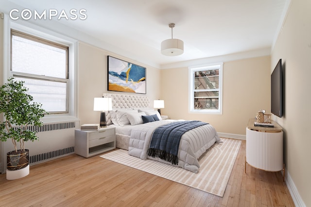 bedroom featuring multiple windows, radiator, baseboards, and hardwood / wood-style floors