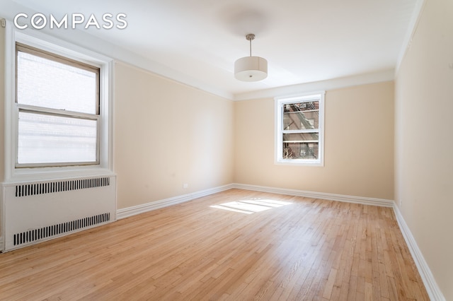 spare room featuring hardwood / wood-style floors, radiator, and baseboards