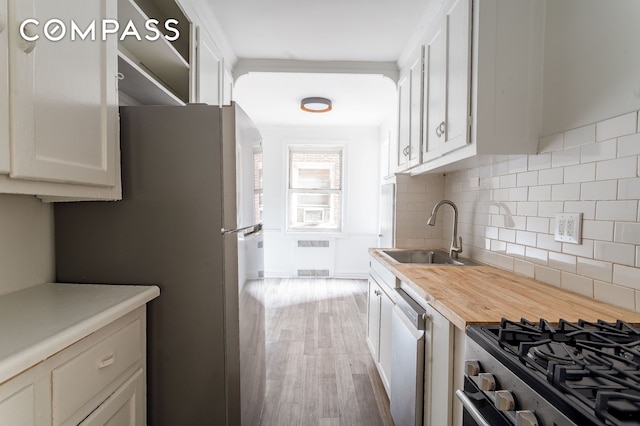 kitchen featuring stainless steel appliances, a sink, wood counters, white cabinetry, and tasteful backsplash