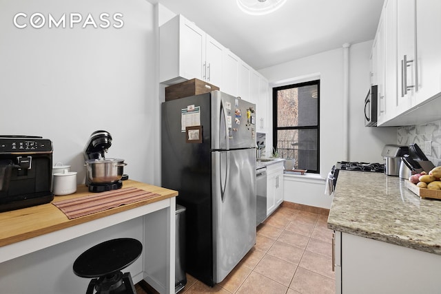 kitchen with stainless steel appliances, light tile patterned floors, white cabinetry, and light stone counters