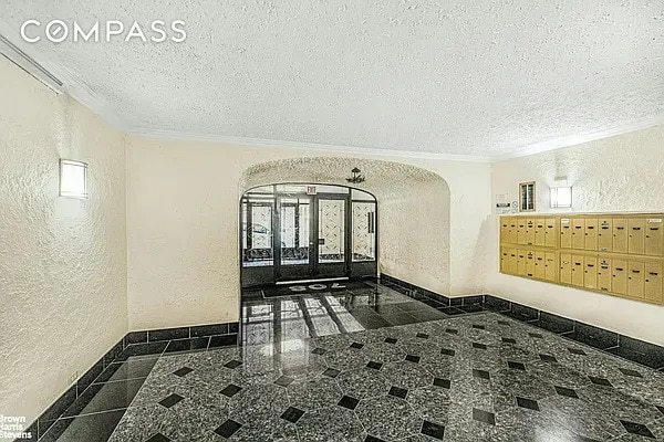 hallway featuring a textured wall, granite floors, inlaid floor details, crown molding, and mail area