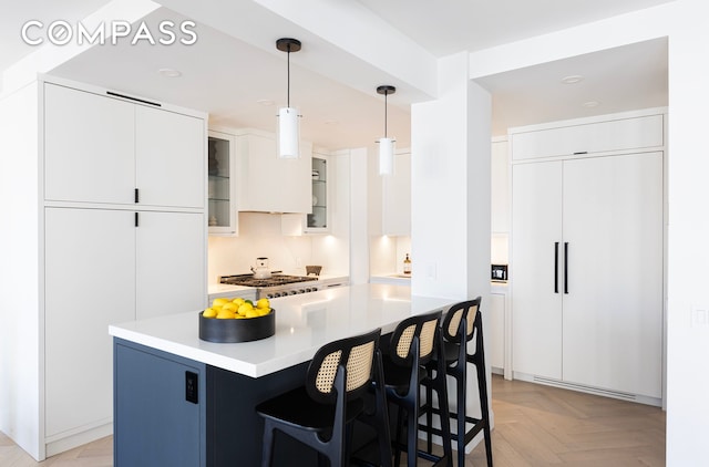 120 E 79th St Unit 15Bc, New York City, NY 10075 - kitchen with a breakfast bar area, glass insert cabinets, white cabinetry, hanging light fixtures, and light countertops