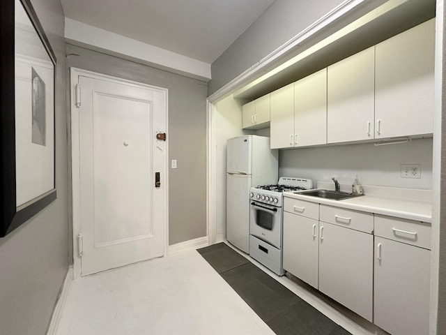 kitchen featuring white appliances, baseboards, a sink, light countertops, and white cabinets