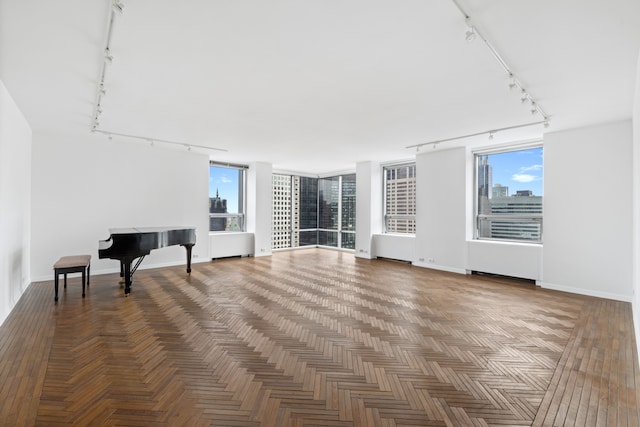 unfurnished living room featuring baseboards, a healthy amount of sunlight, and track lighting