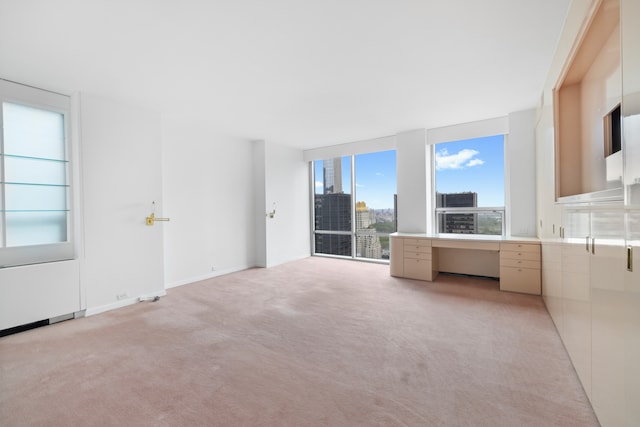 unfurnished living room featuring baseboards, light colored carpet, a city view, and floor to ceiling windows