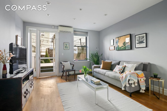 living room featuring light wood-type flooring, baseboards, and a wall unit AC